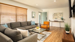 Un salon moderne avec un canapé d’angle, une table basse en verre et un plancher en bois.