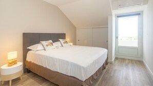 Un dormitorio con una cama grande, una mesita de noche con lámpara, un armario y una ventana con vistas.
