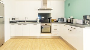 Una cocina moderna con armarios blancos, una campana extractora de acero inoxidable, horno empotrado, microondas, cafetera y un lavabo.