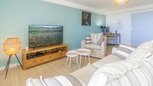 Una sala de estar con televisor de pantalla plana, un sofá, una silla y una mesita.