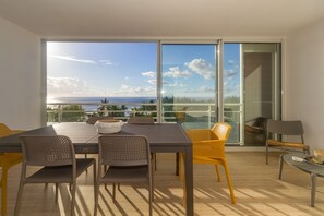 A dining area with a table and chairs, a view of the ocean, and a sliding glass door. - Cap Noir - apt with magnificent sea view - Downtown Saint-Gilles-Les-Bains (Saint-Gilles-Les-Bains)