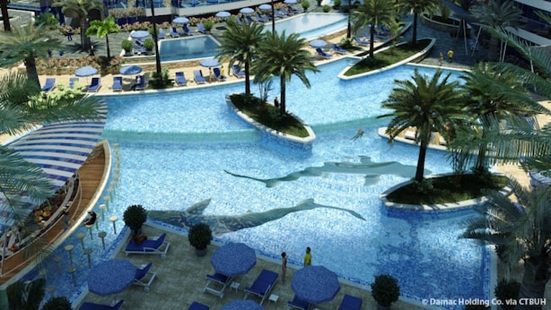 A resort pool area with multiple swimming pools, sun loungers, and palm trees.
