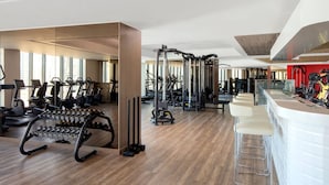 A modern gym with various exercise equipment, a bar area, and a large mirror.