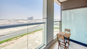 A balcony with a view of a highway and buildings, a table with chairs, and a large window.