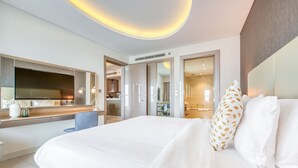 A modern hotel room with a large bed, a flat-screen TV, a desk with a chair, and a bathroom visible through an open door.
