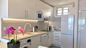 Uma cozinha moderna com armários brancos, micro-ondas embutido, máquina de lavar louça e frigorífico.