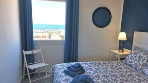 Quarto de hotel com cama, cadeira, mesa de cabeceira, abajur e vista para o mar.