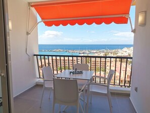 A balcony with a table and chairs, a red awning, and a view of the sea and buildings. - 5mn from the beach: Achacay Standing apartment with sea and mountain views  (Los Cristianos)