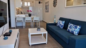 Uma sala de estar moderna com um sofá azul escuro, uma mesa de centro branca e uma área de jantar com cadeiras brancas.