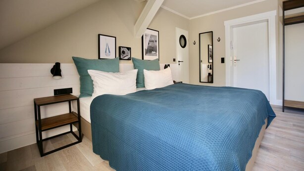 A bedroom with a bed, a nightstand, a wall-mounted lamp, and framed pictures. - Boje06 (Heringsdorf)
