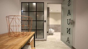 A modern bathroom with a glass door labeled "SAUNA" and a wooden table with a geometric metal basket. - Boje06 (Heringsdorf)