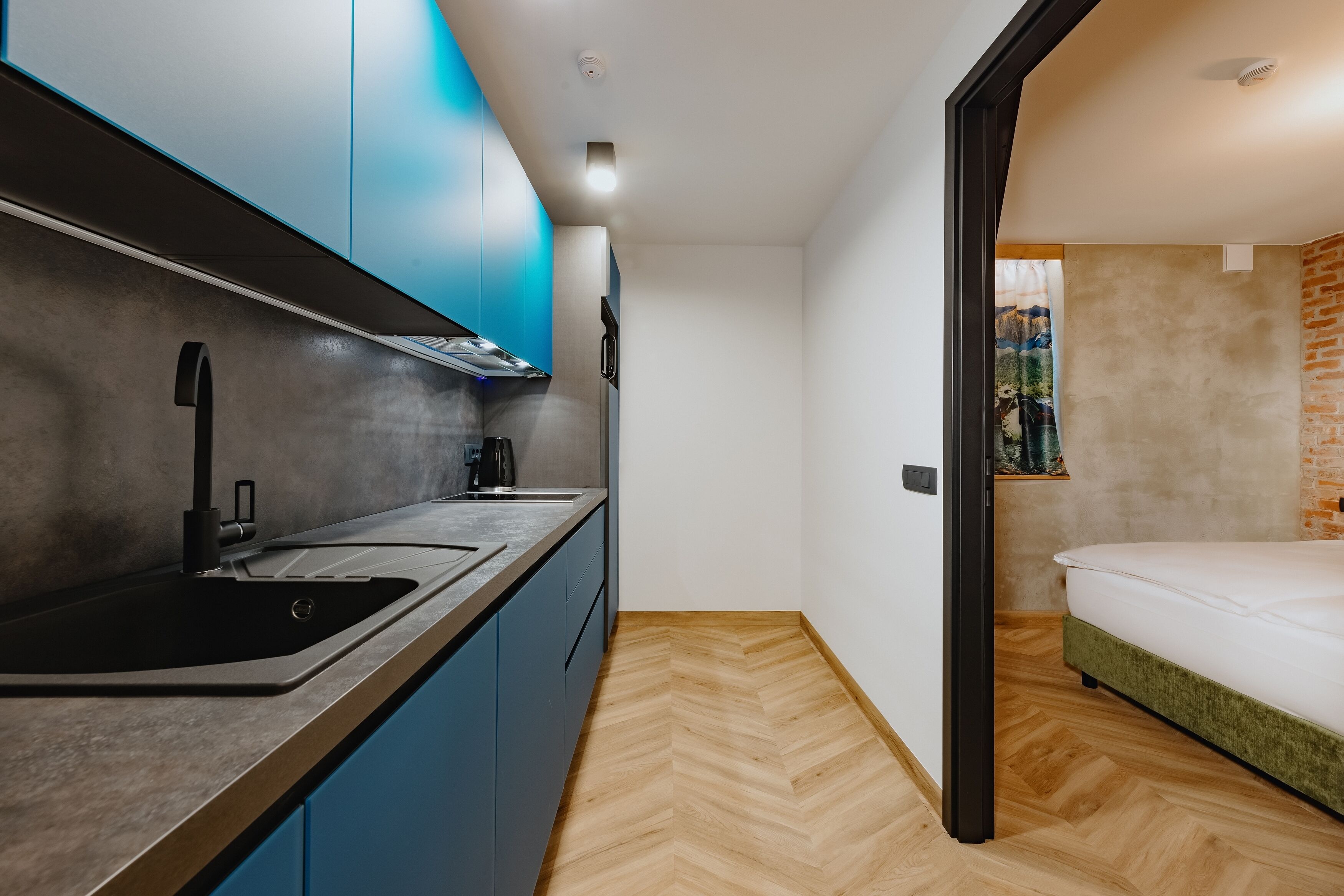 Une cuisine compacte dotée d’un évier moderne, de meubles bleus et d’un parquet en bois disposé en chevrons.