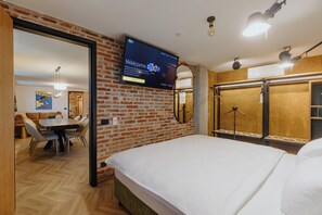Habitación de hotel con pared de ladrillo, una cama, un televisor y un área de comedor con mesa y sillas.