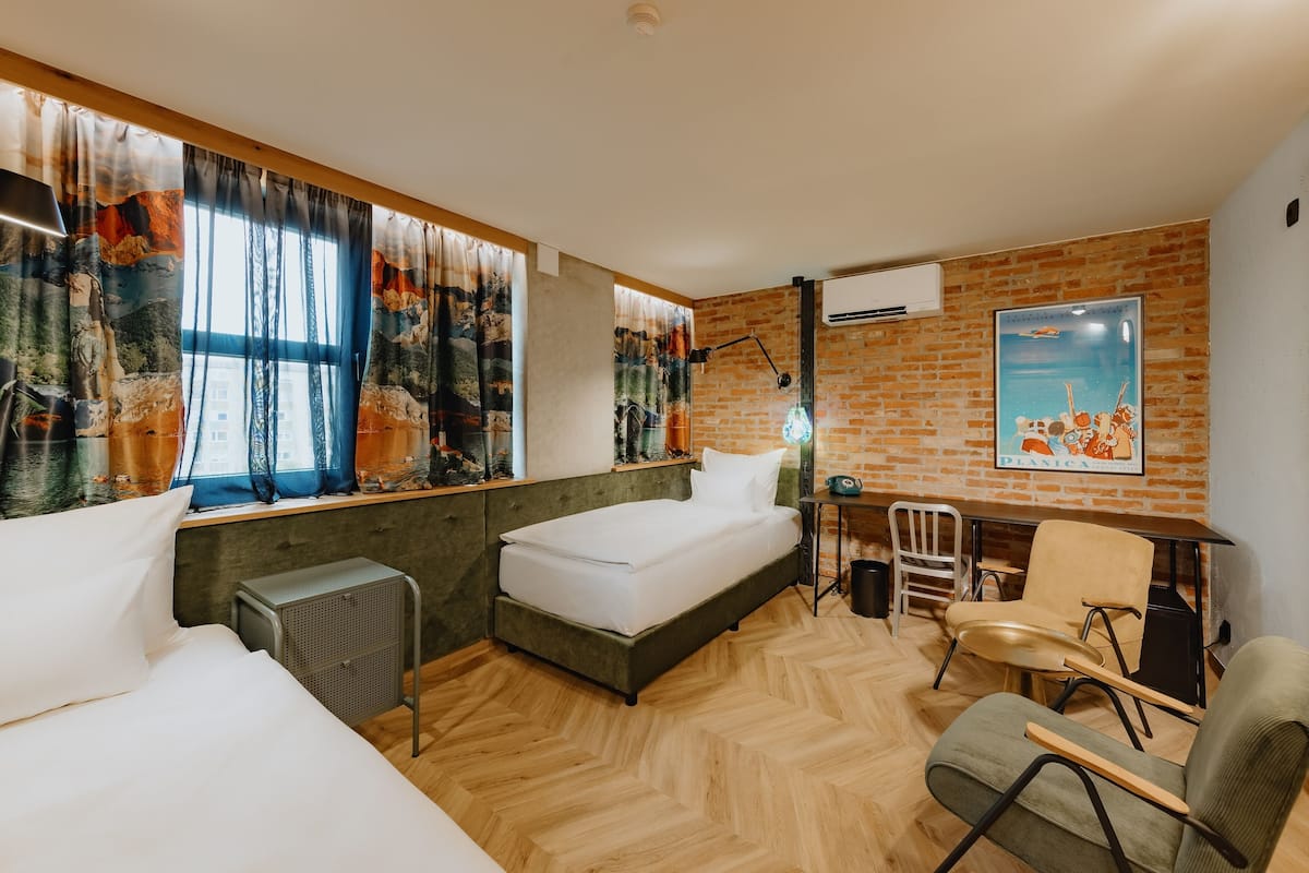 Quarto de hotel com cama, escrivaninha, cadeira e radiador.