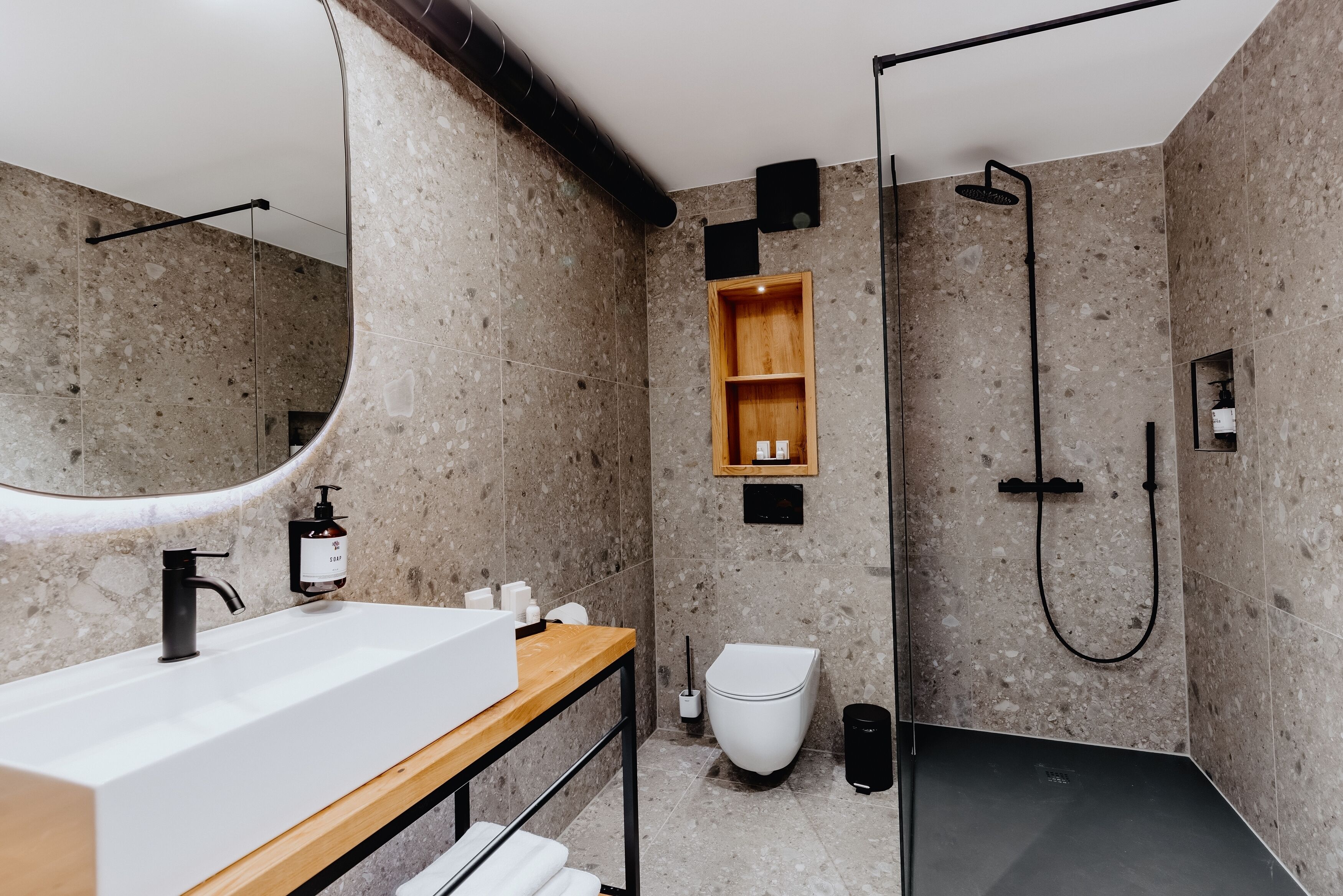 Un baño moderno con un espejo grande, un tocador de madera, un lavamanos blanco, un inodoro y una zona de ducha.