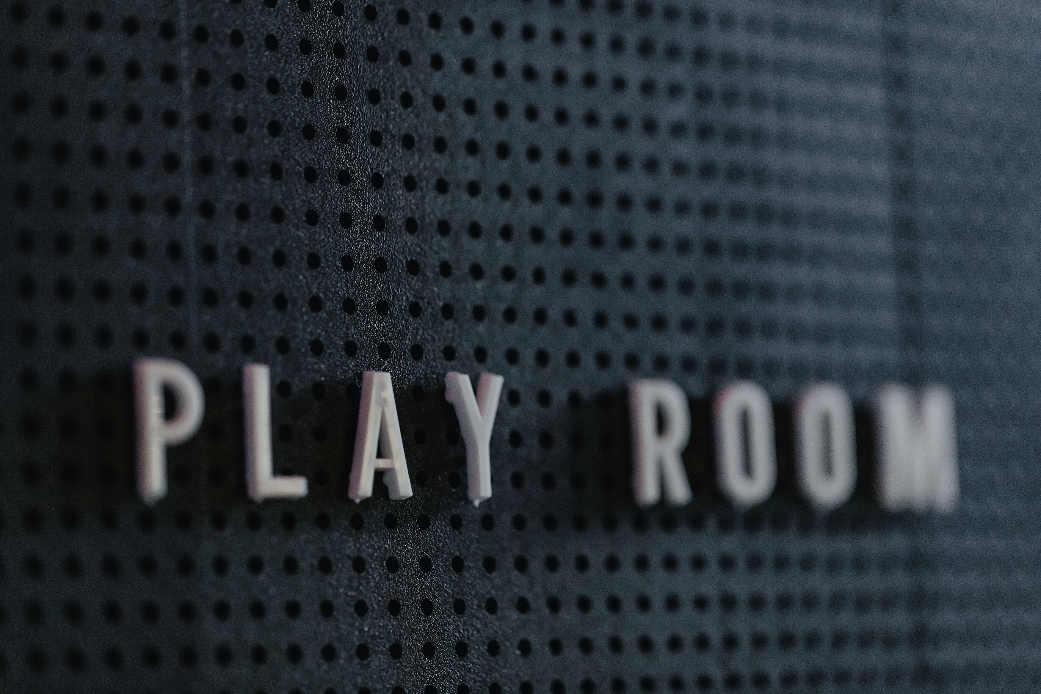 A perforated wall with the words "PLAY ROOM" in white letters.