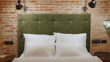 Uma cama com cabeceira estofada verde, almofadas brancas e duas luminárias pretas fixadas na parede.