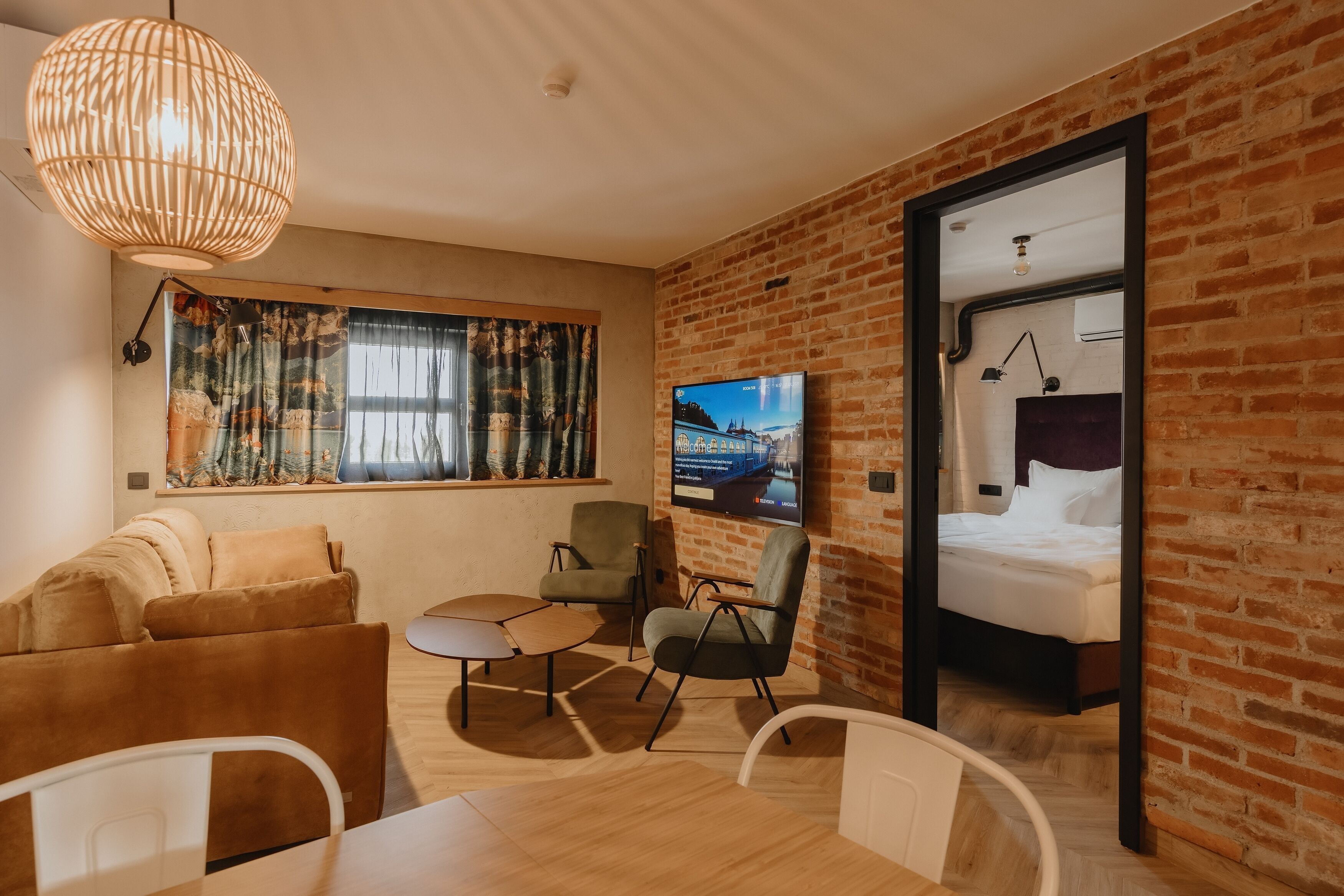 A modern hotel room with a brick wall, a large TV, a sofa, a dining table, and a bed.