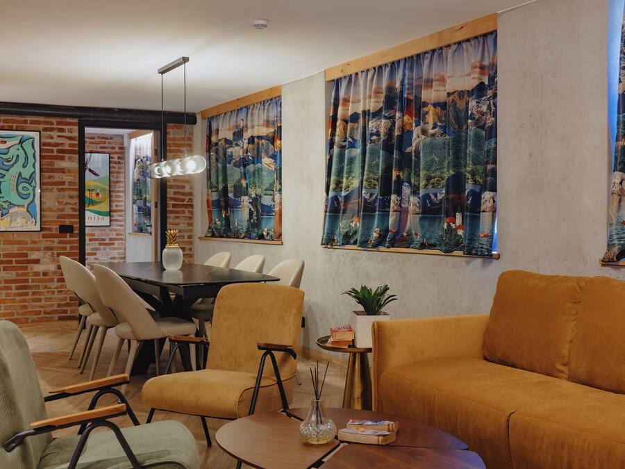 A modern living room with a brick wall, a dining area with a round table and chairs, and large windows with curtains.