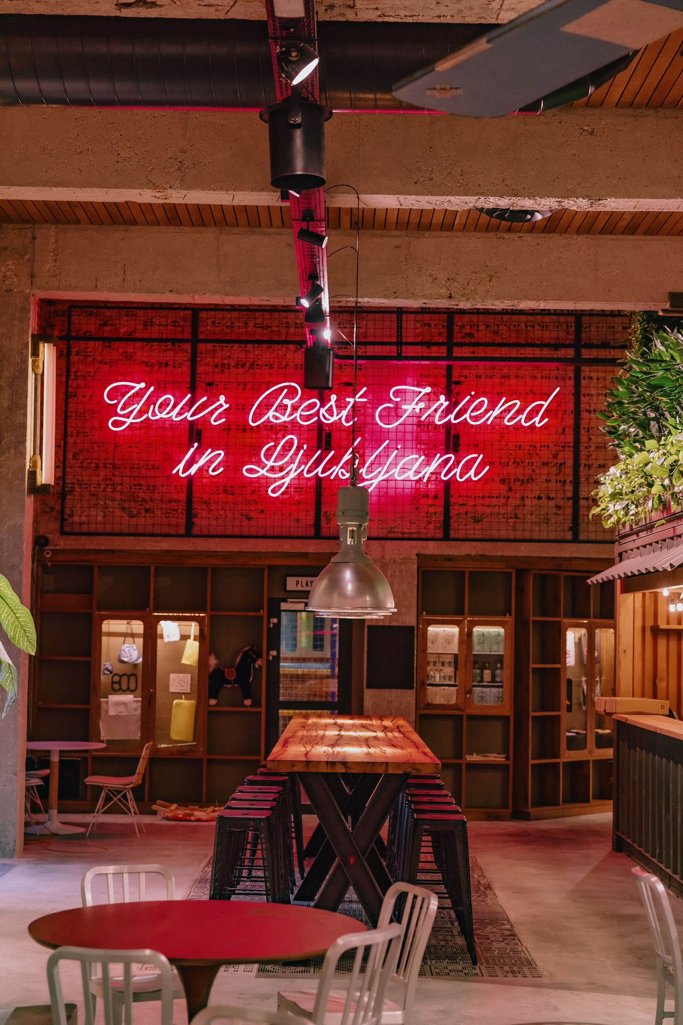 A cozy interior with a neon sign reading "Your Best Friend in Ljusjana," wooden furniture, and a bar area.