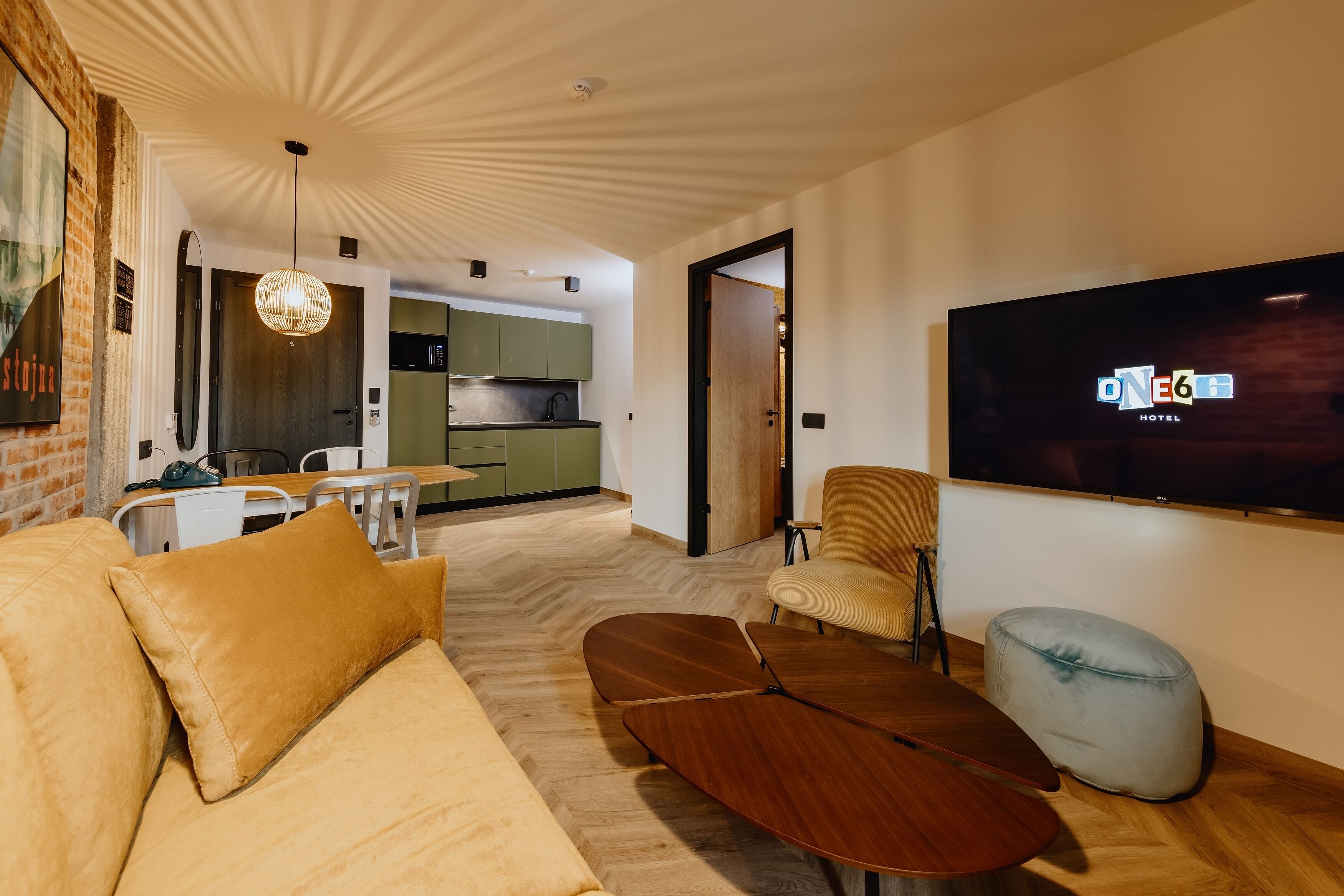 A modern hotel room with a sofa, ottoman, wooden coffee table, and a TV mounted on the wall.