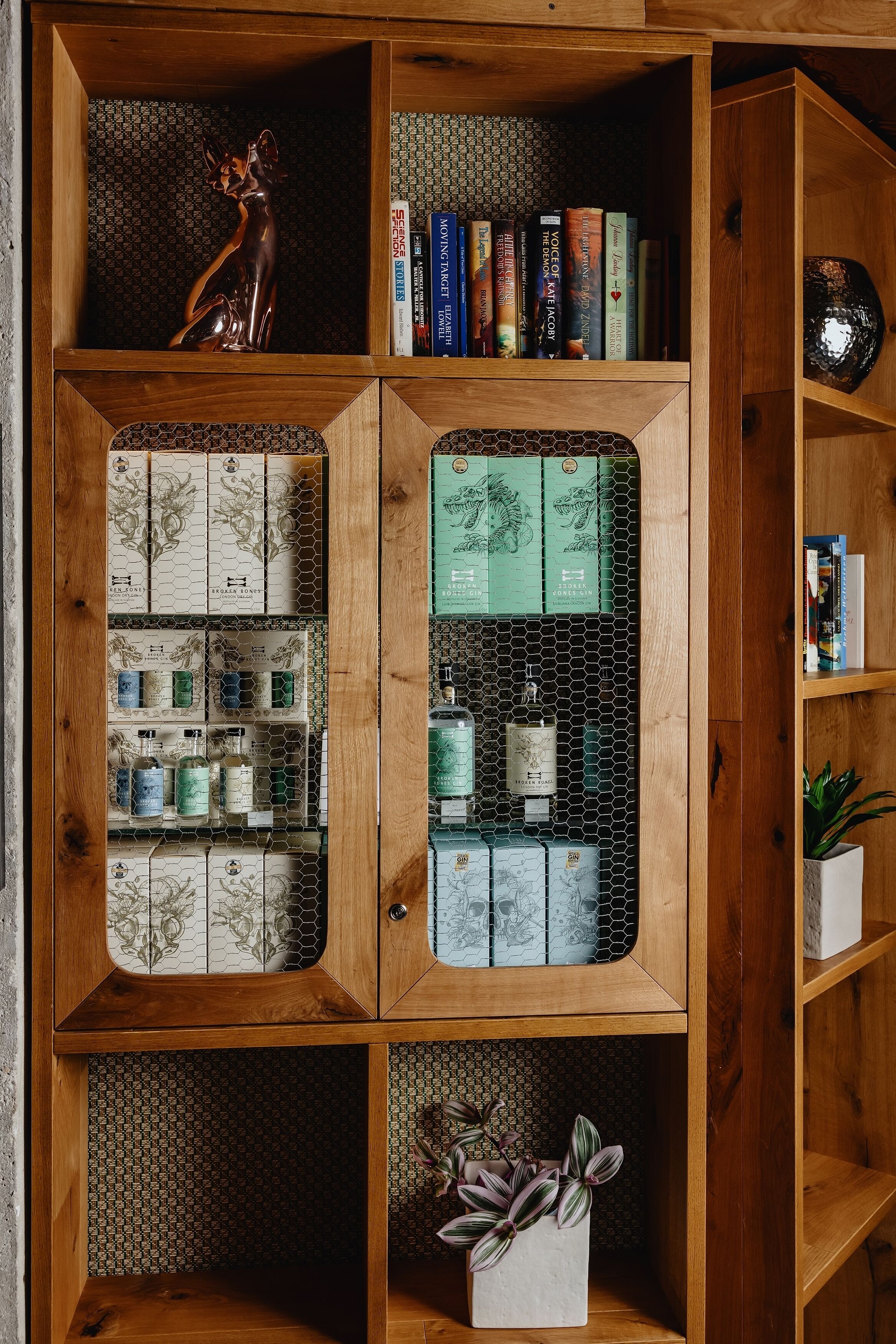Un mueble de madera con varios compartimentos, algunos con libros y otros con cajas y botellas.