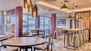 Een moderne eetruimte met ronde tafels, barstoelen, hanglampen en grote ramen met uitzicht op de stad.