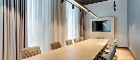 A conference room with a long table, chairs, a flat-screen TV, and curtains.
