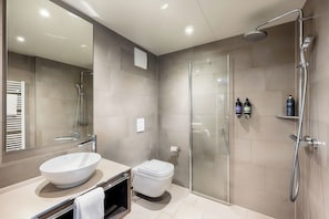 Features a sleek bathroom with a large oval sink, contemporary toilet, and glass-enclosed shower.