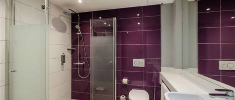 Un baño moderno con cabina de ducha de vidrio, inodoro blanco y lavabo grande.
