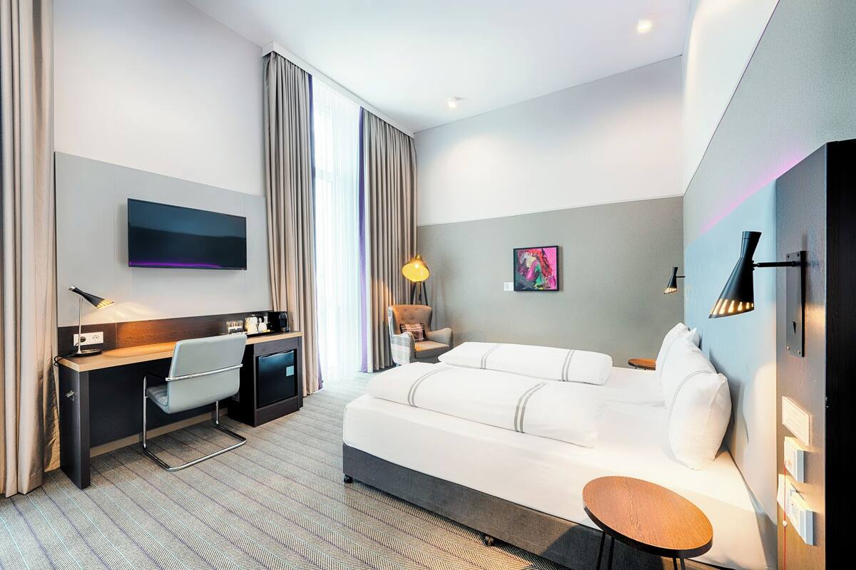 Ein modernes Hotelzimmer mit Bett, Schreibtisch, Stuhl und einem Flachbildfernseher.