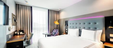 Una habitación de hotel moderna con una cama grande, un escritorio con una silla, una mesita y otra silla.