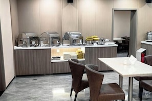 A modern hotel room with a kitchenette, a dining area with a table and chairs, and a view of the hallway.