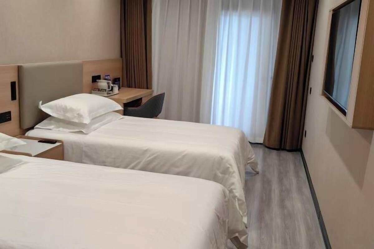 A hotel room with two beds, a desk, a chair, and a window with curtains.