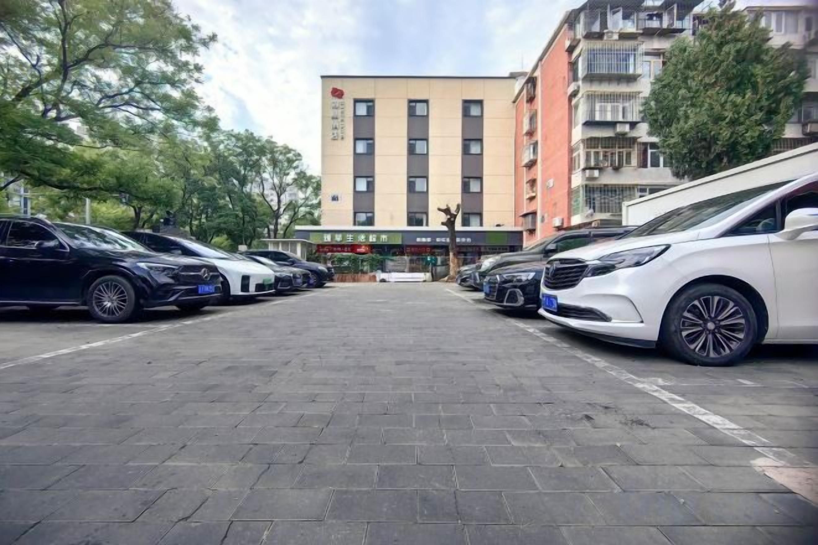 Parkkipaikka, jossa on useita autoja, monikerroksinen rakennus, jossa on useita ikkunoita, ja kirkas taivas.