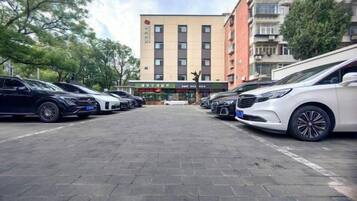 Parkkipaikka, jossa on useita autoja, monikerroksinen rakennus, jossa on useita ikkunoita, ja kirkas taivas.