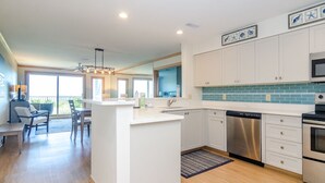 A modern kitchen with white cabinetry, a central island, stainless steel appliances, and a blue backsplash. - Upgraded Oceanfront 3BR Condo in WrightsvilleDunes (Wrightsville Beach)
