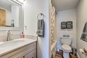 Un baño con lavamanos blanco, espejo y váter. Hay toallas colgadas en la pared y una cortina de ducha.