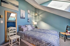 Un dormitorio con tragaluz, cama con colcha estampada, una silla y decoración en la pared.