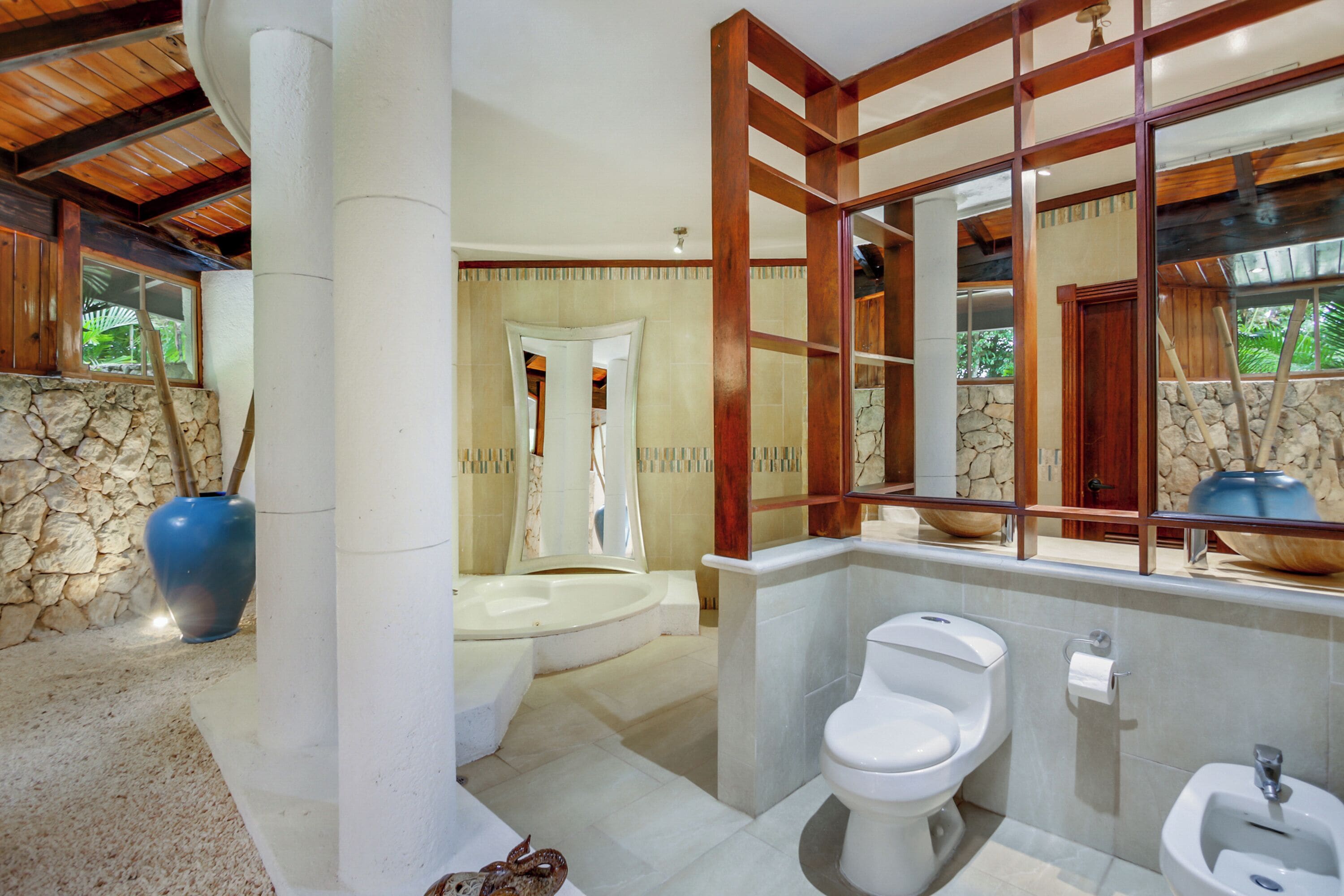 A bathroom with a stone wall, a bathtub, a toilet, and a bidet.