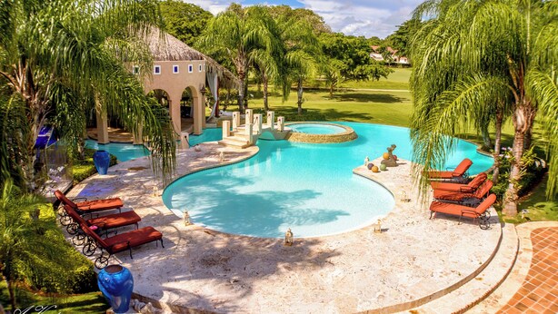 A pool area with lounge chairs, a thatched-roof structure, and palm trees. - 5-star villa for rent in Moroccan-style (La Romana)