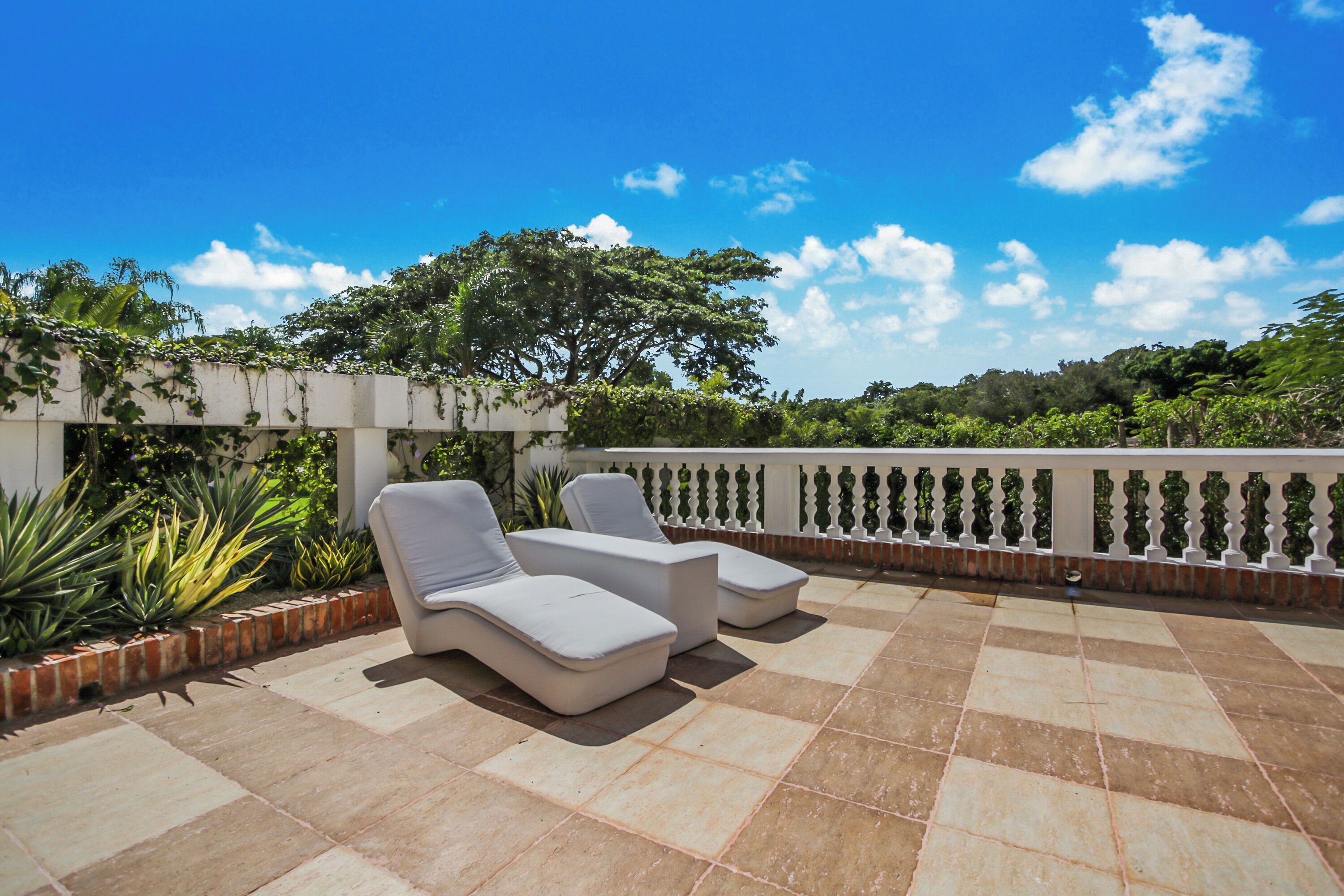 A rooftop terrace with two white lounge chairs, a tiled floor, and a white balustrade.