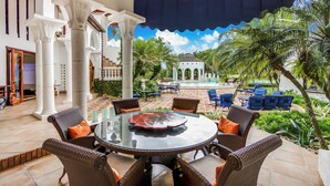An outdoor patio with a round table, wicker chairs, and a view of a pool and palm trees. - 5-star villa for rent in Moroccan-style (La Romana)