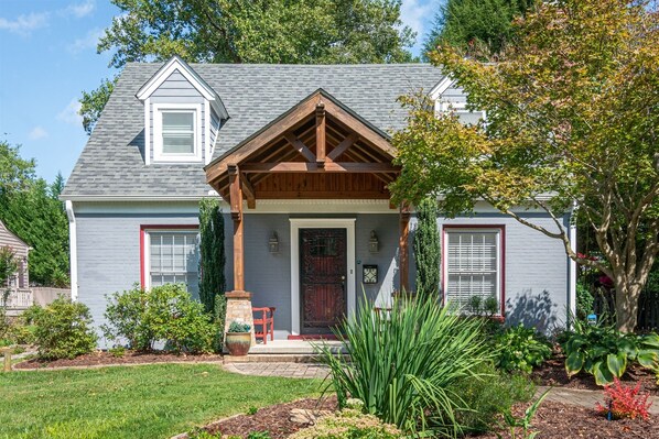 Stunning two-story house with a gabled roof and inviting front porch, surrounded by a beautifully manicured lawn and lush greenery.