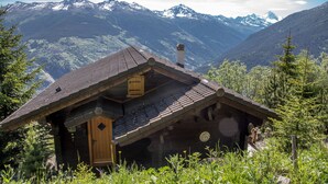 A wooden cabin with a sloped roof, a chimney, and a door, surrounded by lush greenery and mountains in the background. - This stunning, bright and comfortable chalet can accommodate up to 8 people. Located on the Chemin d (Les Masses)