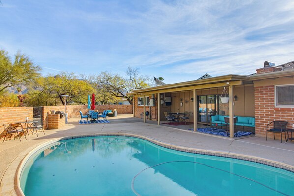 A swimming pool with a covered patio area, outdoor furniture, and a brick wall. - Private Pool & Fire Pit! Walkable Tucson Retreat (Tucson)