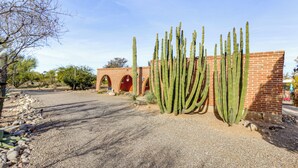 Um edifício com fachada de tijolos e portas em arco, cercado por um caminho de cascalho e cactos.