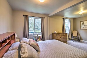 Quarto com uma cama grande, cômoda de madeira, uma cadeira e janela com cortinas.