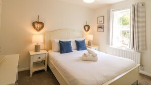A neatly arranged bedroom with a large bed, two bedside tables with lamps, heart-shaped wall decorations, and a window with curtains.