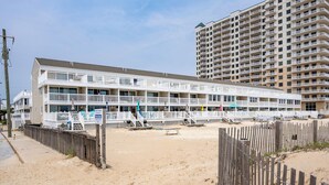 Et hotel ved stranden med flere balkoner, et sandbad og et træhegn.